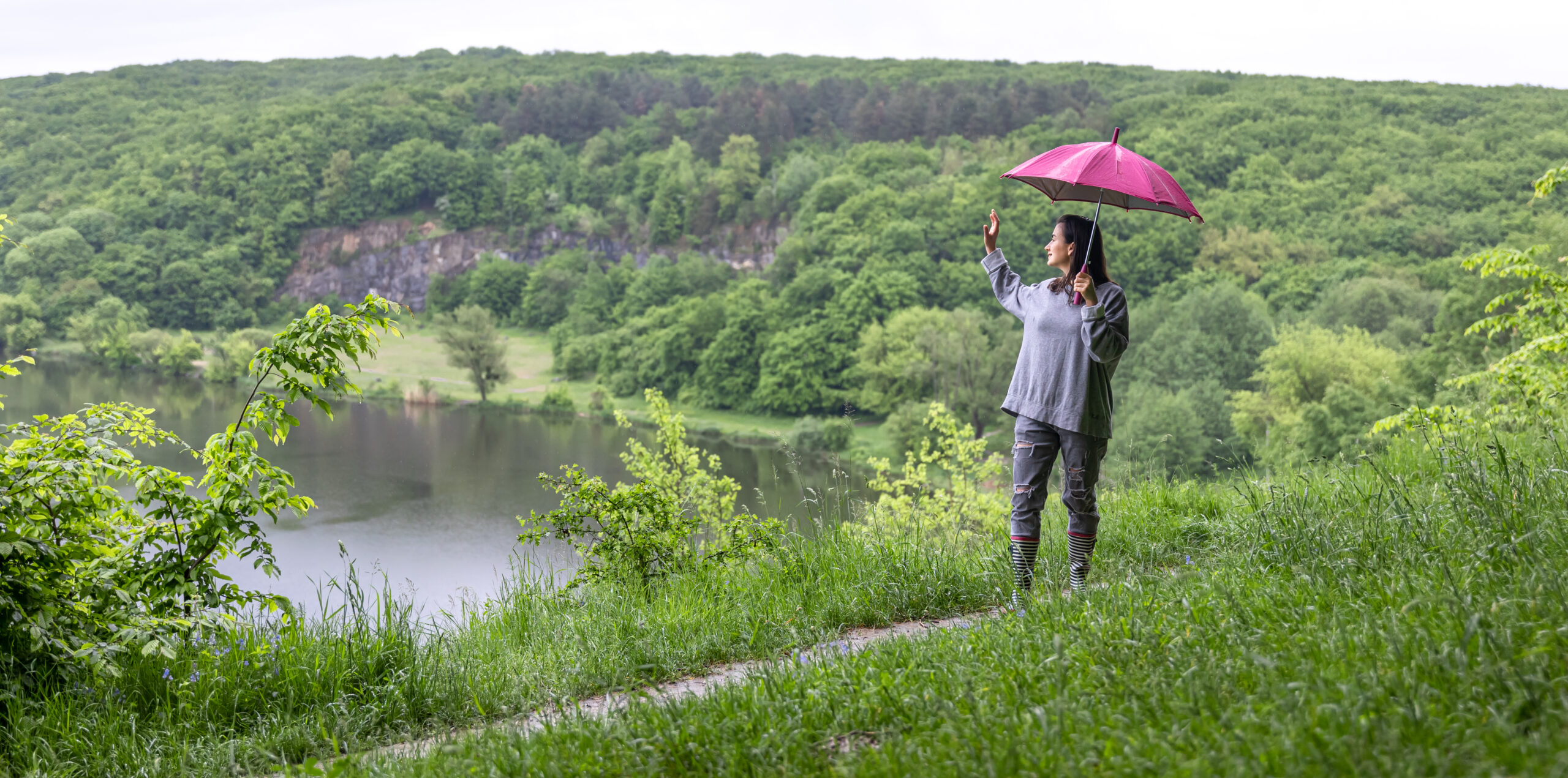 A girl on a walk in the forest under an umbrella among the mountains near the lake.